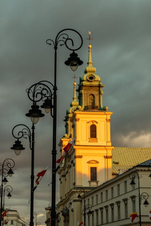 From below of aged Holy Cross Church located on street near vintage lanterns under cloudy sunset sky in Warsaw