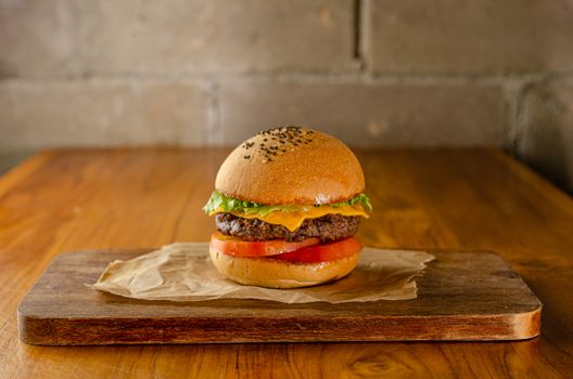 Delicious cheeseburger with lettuce, tomato, and cheese on a wooden board.