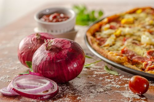 Free Red onions and fresh tomatoes arranged near a delicious pizza, ideal for food photography. Stock Photo