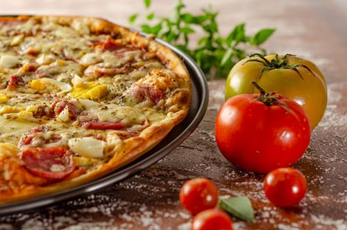 Free Delicious pizza topped with veggies and cheese, accompanied by fresh tomatoes on a rustic table. Stock Photo