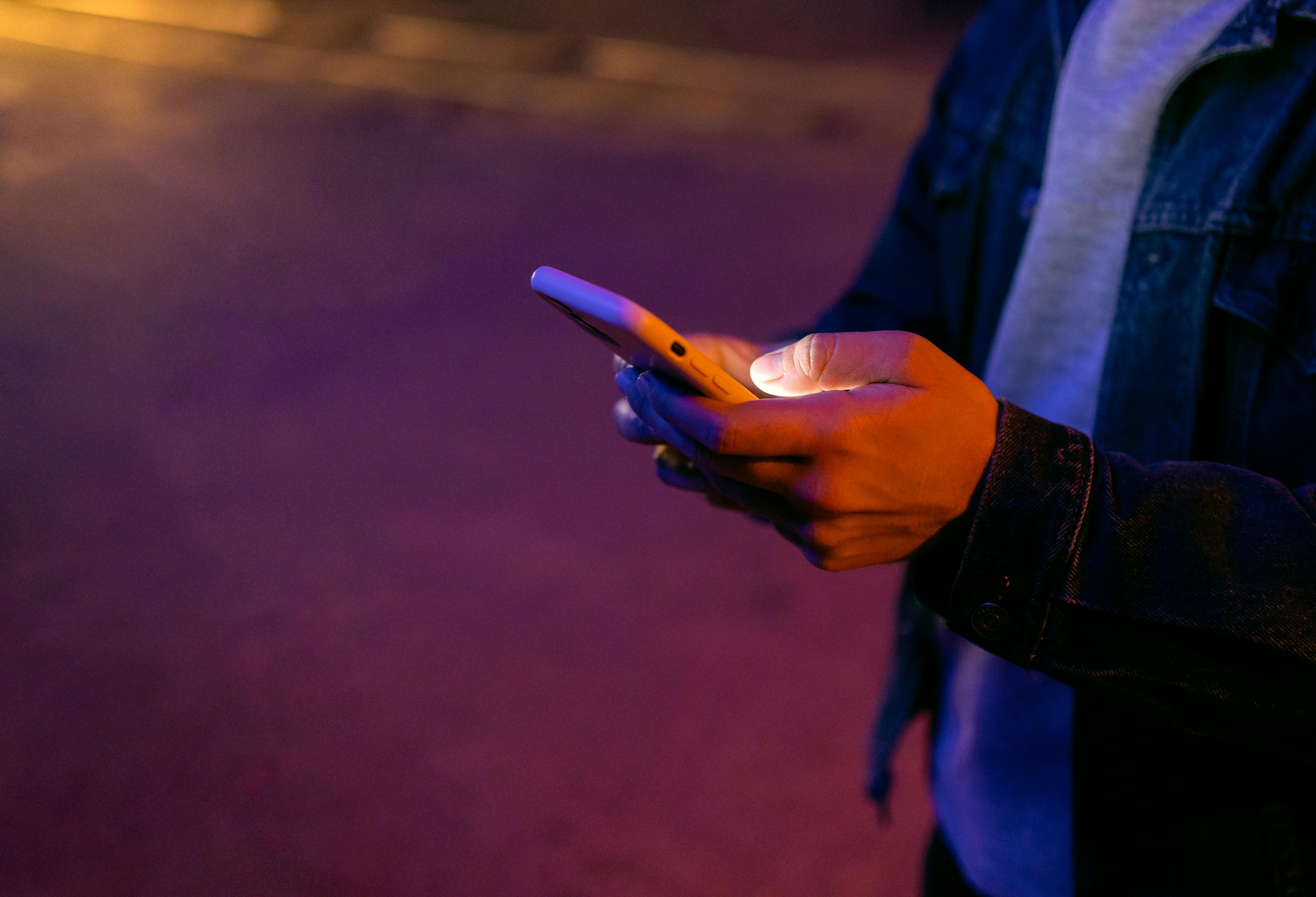 夜晚，一个人手持智能手机站在户外，被彩色的环境灯照亮