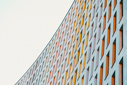 Low angle of gray cloudless sky over tall majestic light blue contemporary building with lots of multi colored windows