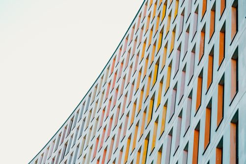 Free Low angle of gray cloudless sky over tall majestic light blue contemporary building with lots of multi colored windows Stock Photo