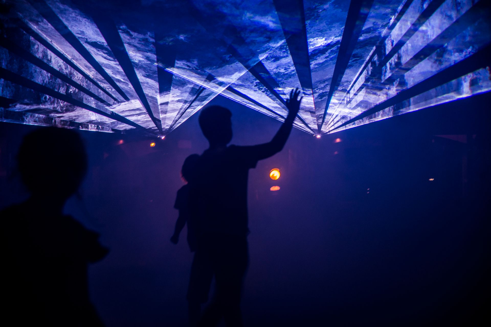 Silhouette of people interacting with an artistic indoor light display, creating a mesmerizing visual effect.