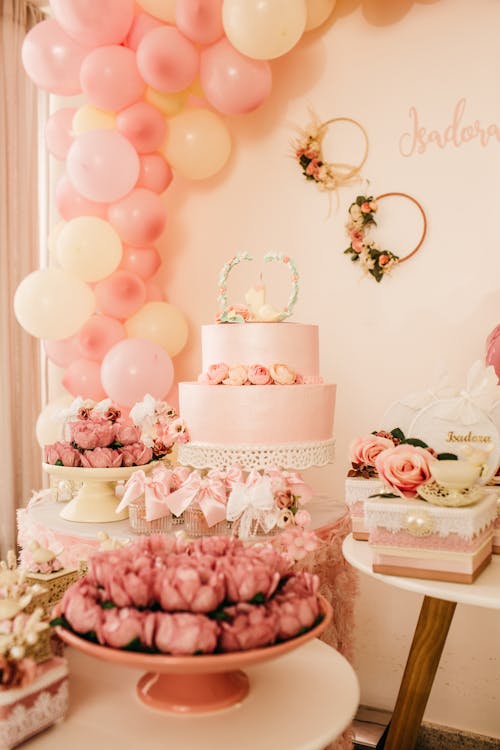 Appetizing desserts near wedding cake decorated with flowers and balloons on pink wall