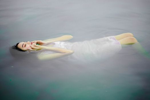 Side view of unemotional ethnic female in dress touching face with eyes closed while resting in reservoir in daytime