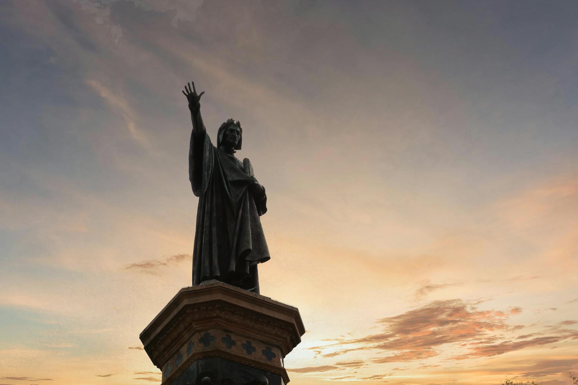 Majestic statue of Dante Alighieri silhouetted against a stunning sunset sky in Trento, Italy.