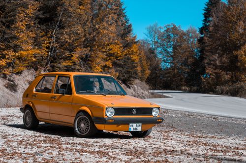 Free A classic yellow car parked on a scenic road surrounded by autumn foliage, showcasing a nostalgic travel vibe. Stock Photo
