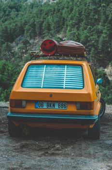 A vintage yellow car parked in a forest with luggage on its roof, perfect for travel themes.