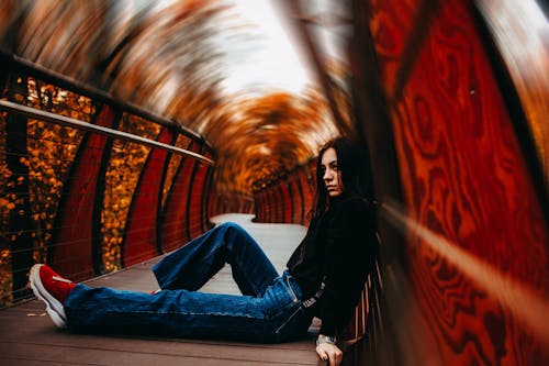 Free Woman in Black Jacket and Blue Denim Jeans Sitting On A Walkway Stock Photo