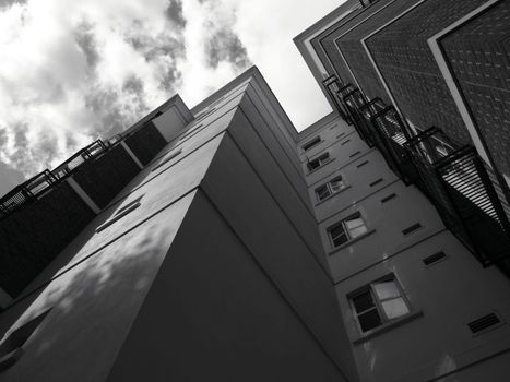 Black and white low angle view of modern buildings against a cloudy sky. Architectural symmetry in urban setting.
