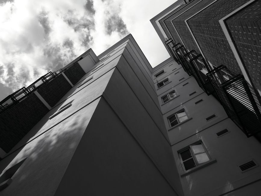 Black and white low angle view of modern buildings against a cloudy sky. Architectural symmetry in urban setting.
