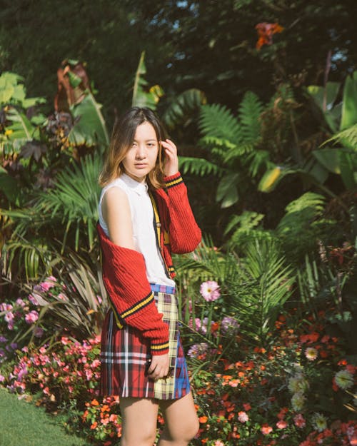 Free Woman in White Tank Top and Red and Black Plaid Skirt Standing Near Green Plants Stock Photo