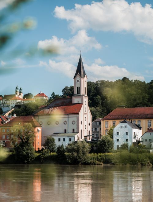 Free Beautiful riverside townscape with church, colorful buildings, and lush greenery. Stock Photo
