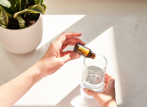 Hands pouring doterra Litsea essential oil into a glass of water, next to a potted plant.