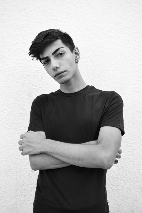 Free Striking grayscale portrait of a young man with arms crossed against a textured background. Stock Photo