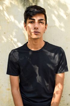 一名穿着黑色衬衫的年轻人自信地靠在户外纹理墙壁上摆姿势