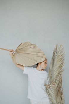 一名女子手持干棕榈叶，以灰色背景为衬托，展现出极简主义风格