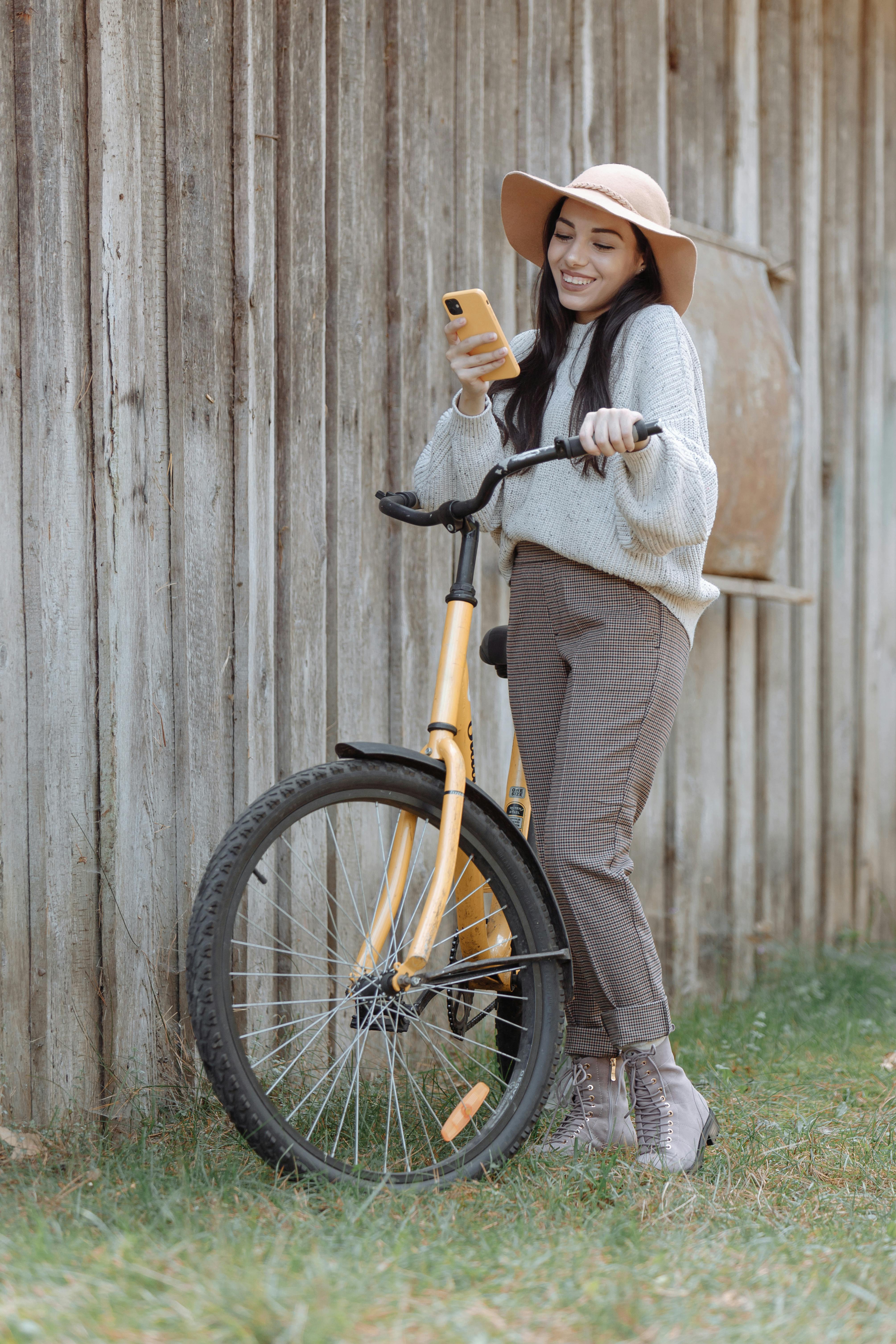 Woman leaning on a bicycle, smiling at a smartphone outdoors on a sunny day.