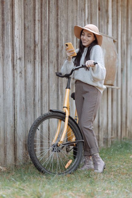 Woman leaning on a bicycle, smiling at a smartphone outdoors on a sunny day.