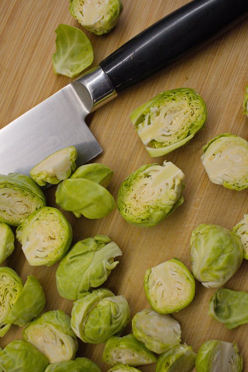 Top view of sharp knife and halved Brussels sprouts placed on cutting board
