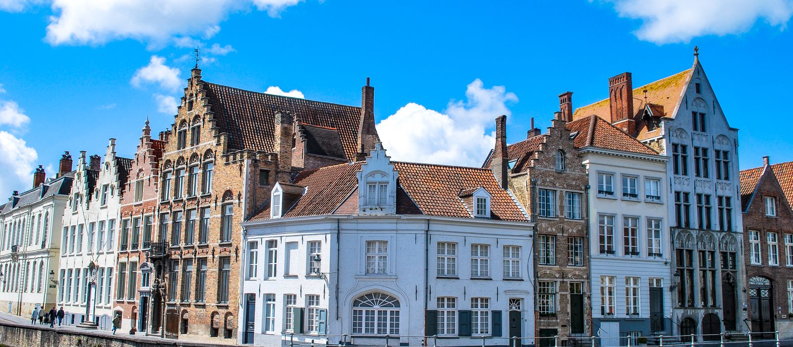 Charming townhouses along a canal in Bruges, Belgium under a vibrant blue sky.