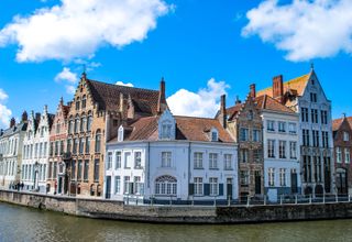 Charming townhouses along a canal in Bruges, Belgium under a vibrant blue sky.