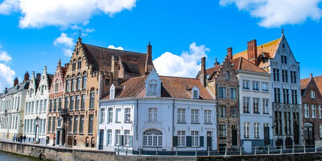 Charming townhouses along a canal in Bruges, Belgium under a vibrant blue sky.