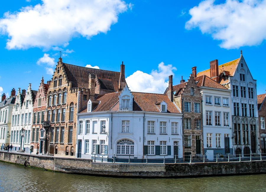 Charming townhouses along a canal in Bruges, Belgium under a vibrant blue sky.