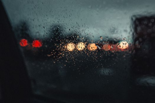 夜晚，车窗上的雨点模糊了城市的灯光，营造出一幅忧郁的景象