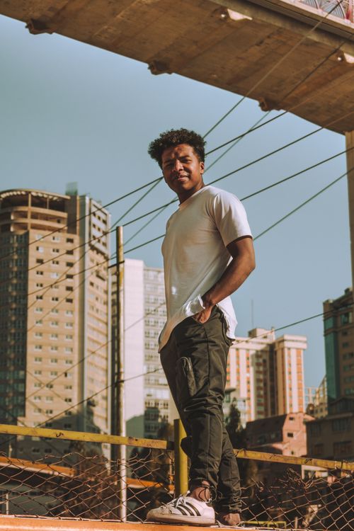 Free A young man stands confidently in an urban environment, wearing a white t-shirt and sneakers. Stock Photo