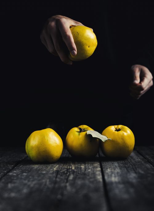 Free Faceless person in darkness holding quince above shabby table with fruit in studio Stock Photo