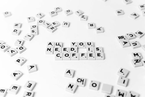 Free Scrabble tiles spell out 'All You Need Is Coffee' on a white background, offering a creative still life. Stock Photo