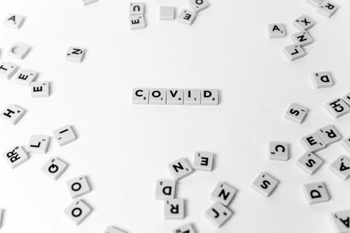 Free Scrabble tiles spelling out COVID on a white surface, representing the pandemic concept. Stock Photo
