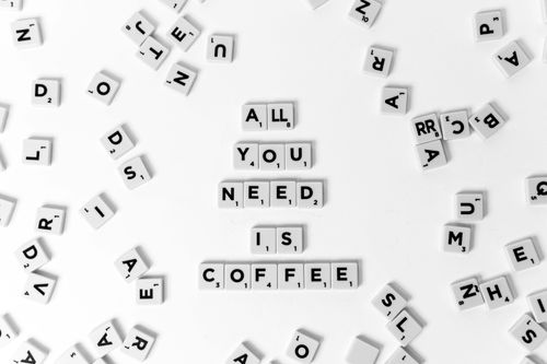 Free Creative arrangement of Scrabble tiles spelling 'All You Need is Coffee' on a white background. Stock Photo