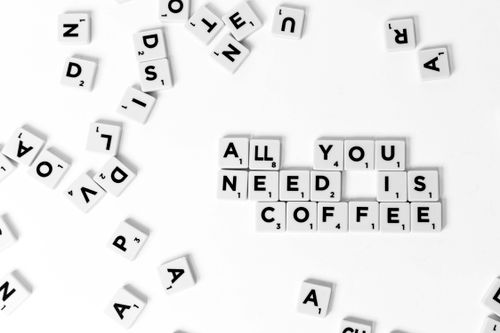 Free Scrabble tiles spell 'All You Need is Coffee' on a white surface, emphasizing creativity. Stock Photo