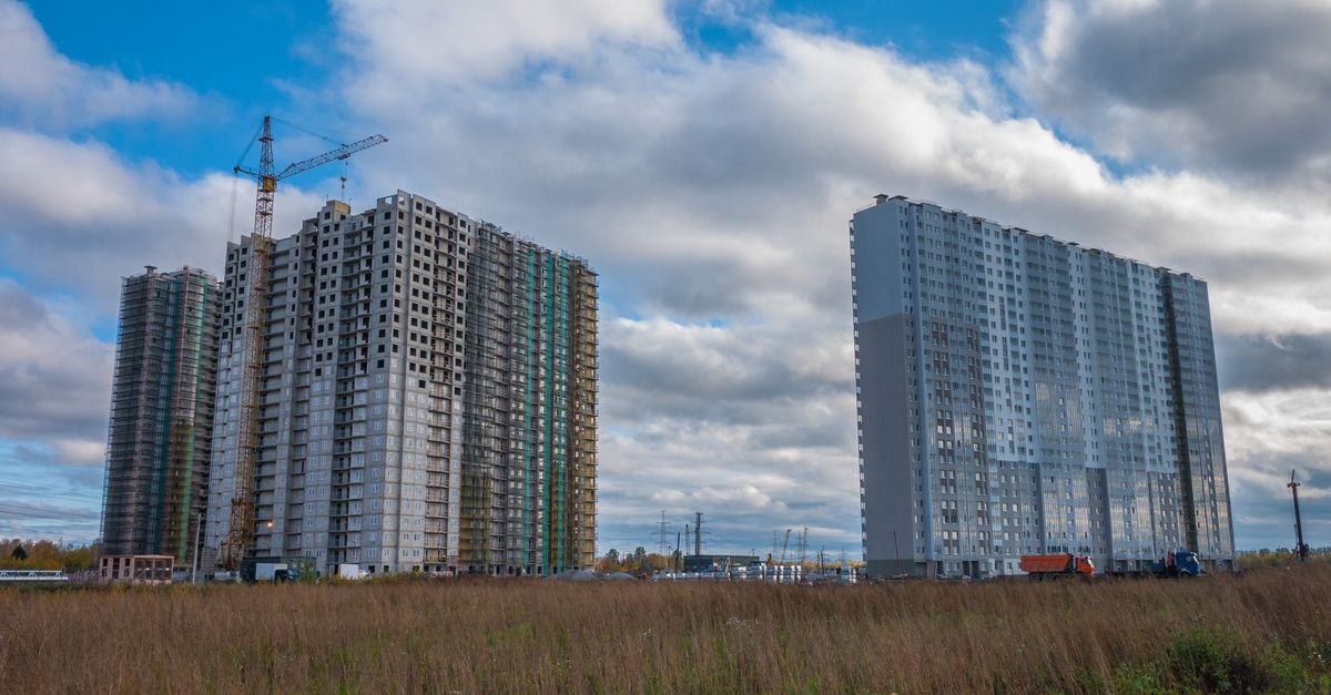 Two high-rise buildings under construction with cranes against a blue sky.