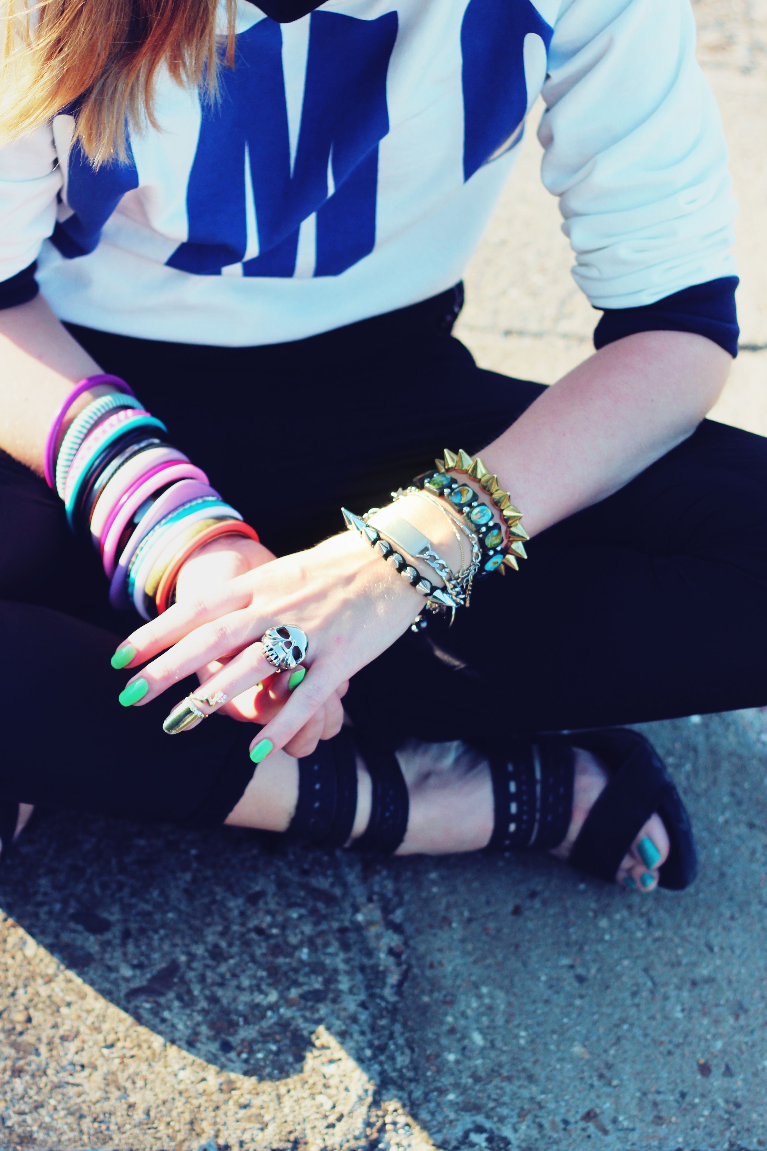 Mulher antenada na moda exibindo pulseiras vibrantes e anéis ao ar livre em um dia ensolarado.
