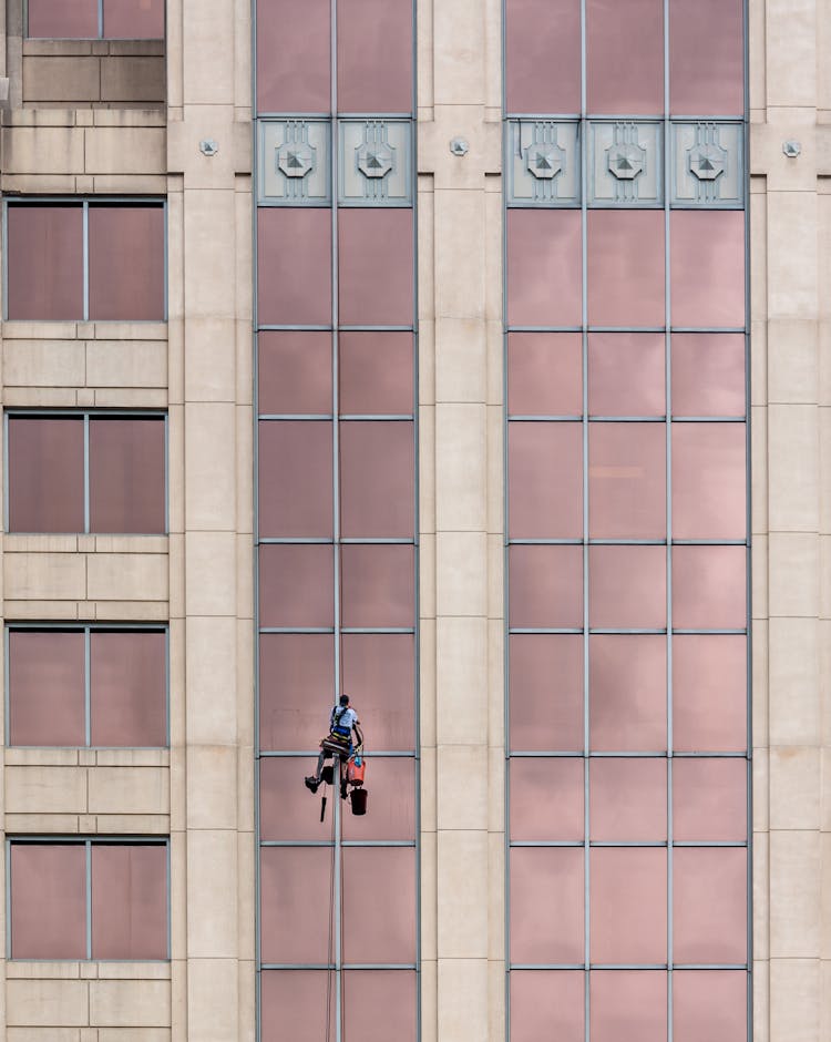 Man Hanging From A Building Cleaning The Glass Windows 