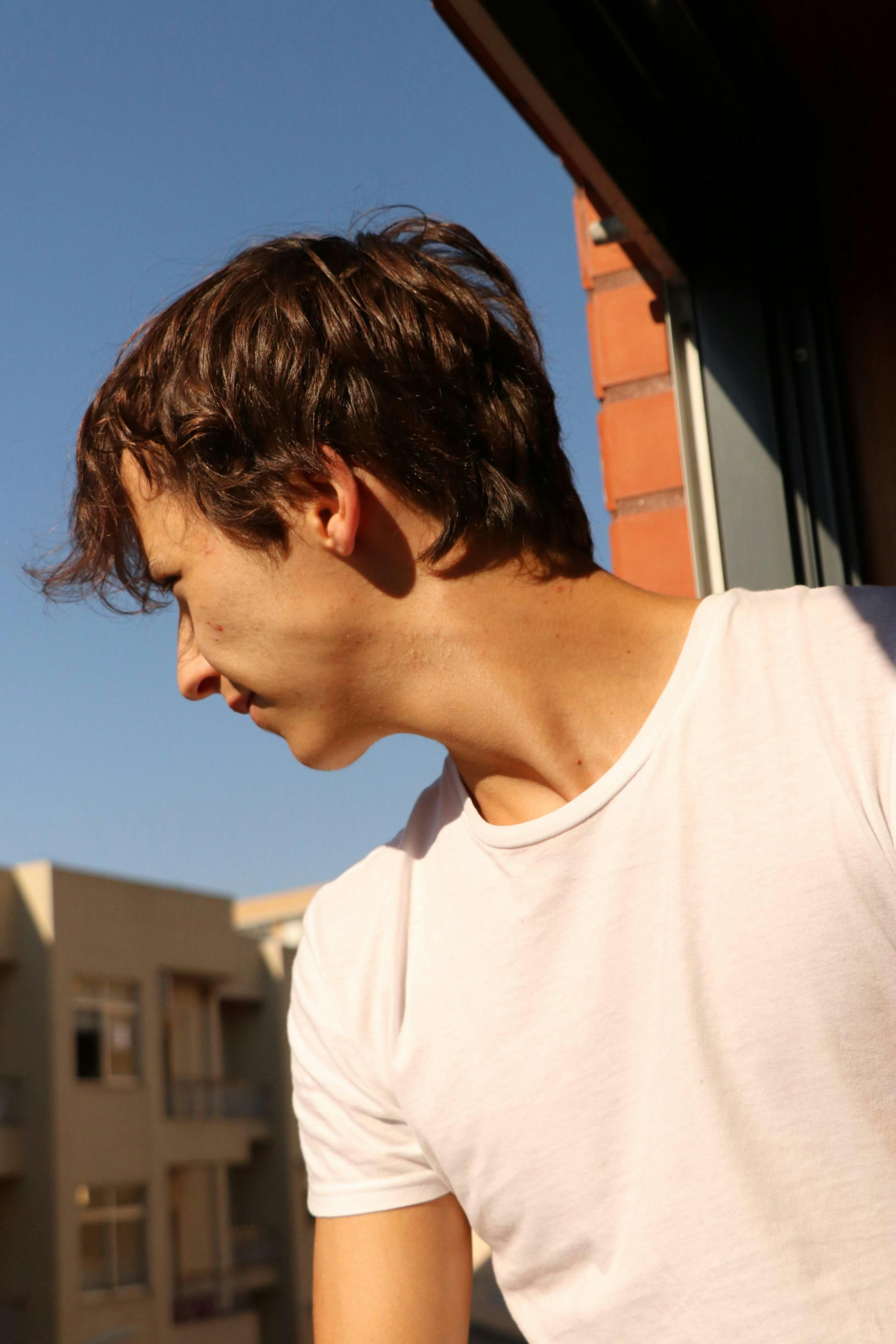 Side view of a young man in a white shirt looking outside from a building balcony.