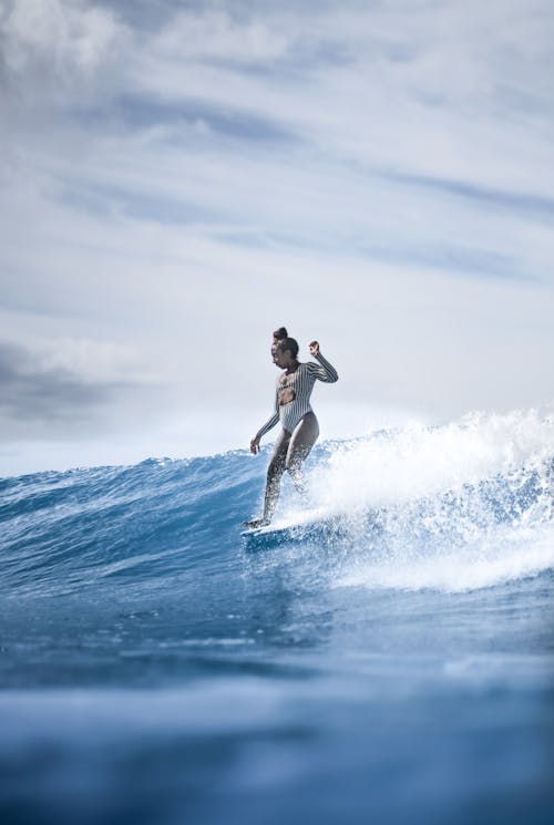 Full length fit female in white swimwear surfing board on foamy sea waves under clear blue skies on sunny weather