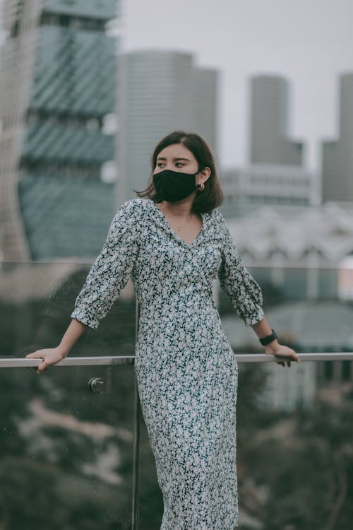 Stylish woman in mask standing near building glass railing