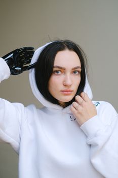 一位身穿白色连帽衫的女士在室内自信地摆着姿势，展示她的仿生假肢