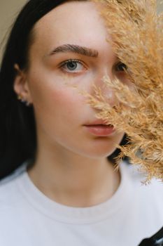 一位深色头发、穿着休闲服的迷人女性，在白天用干树枝遮住脸看向镜头