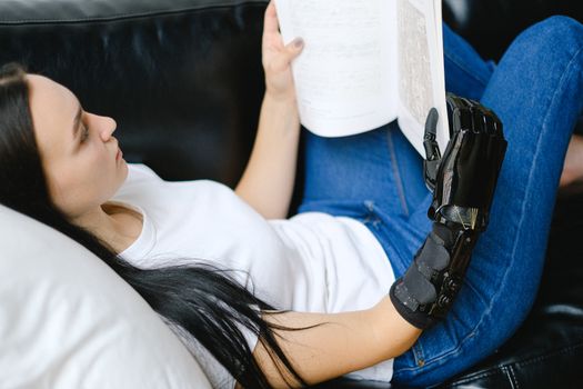 一名拥有仿生手臂的女子在室内沙发上放松身心，正在读书