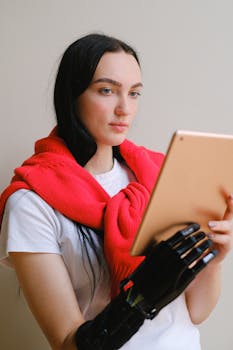 A woman with a prosthetic arm uses a digital tablet indoors, showcasing modern technology and inclusivity.