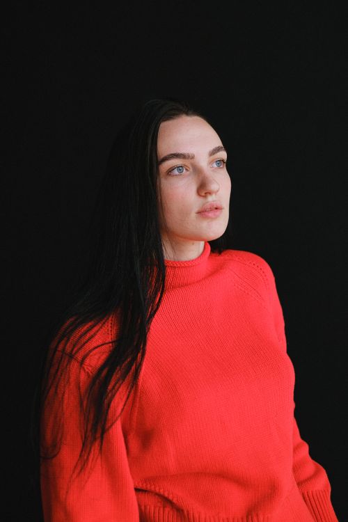 Free Calm woman with long black hair in bright red sweater pensively looking away against black background in daytime Stock Photo