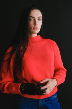 一名女子穿着红色毛衣，在黑暗背景下用仿生假手摆姿势