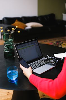 A woman works on her laptop and smartphone at home, multitasking in a cozy living room.