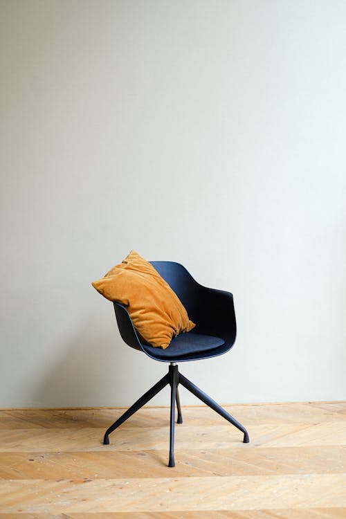 Stylish comfortable chair with soft yellow pillow placed on wooden parquet against light wall in spacious room in daytime